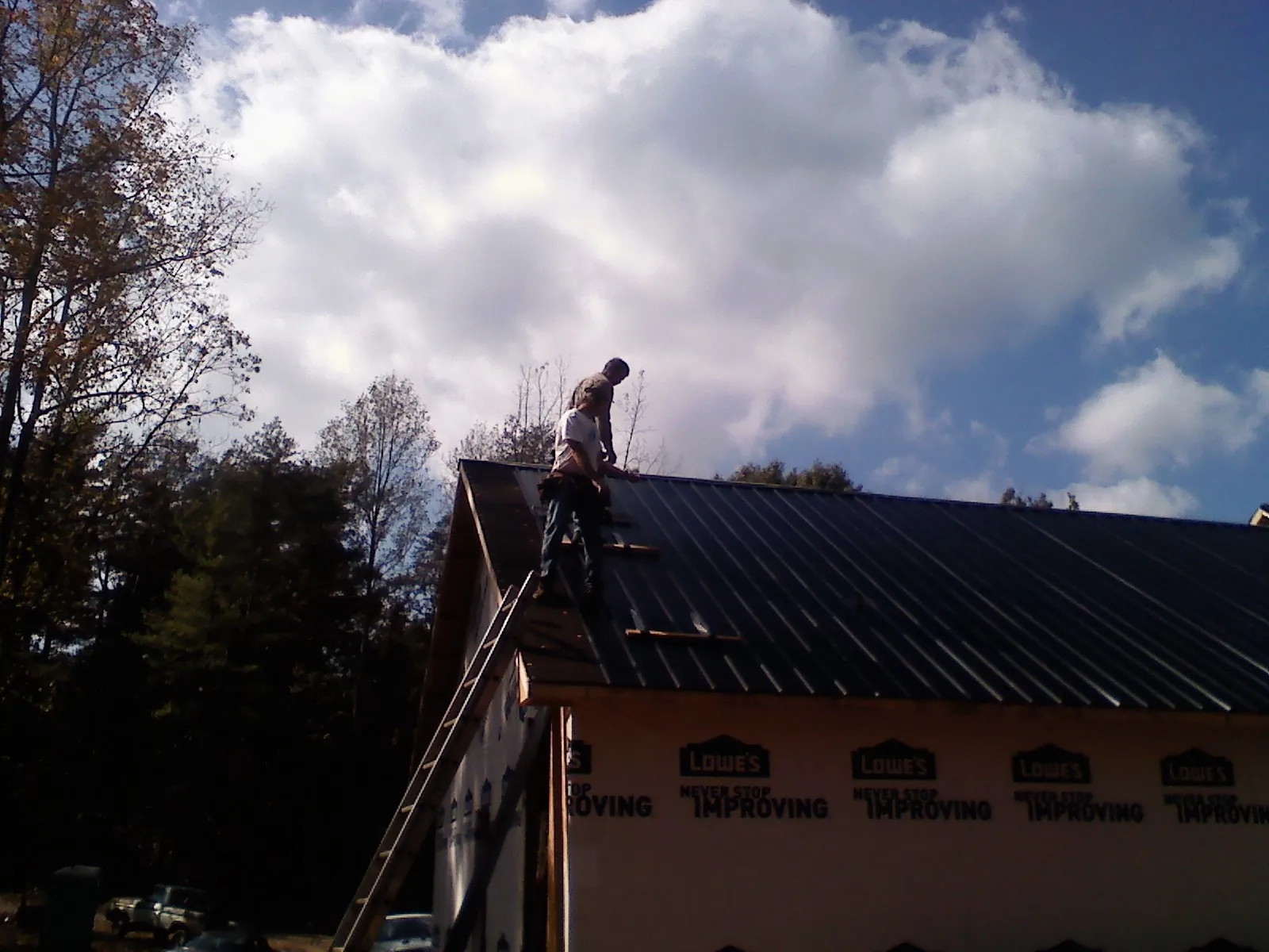 Roofer fastening dark metal panels high against a cloudy sky, from a Roof Inspection job in Clearfield