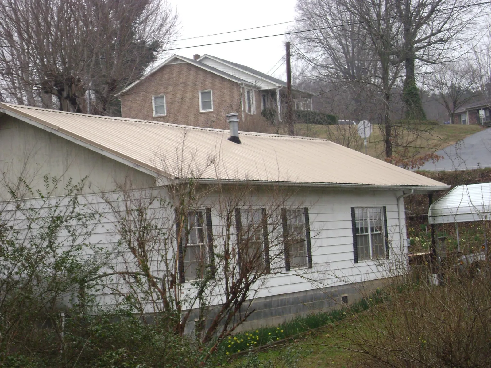 Tan metal roof on a white sided house set into a hillside — Commercial Roofing by Roofing Brothers in Clearfield